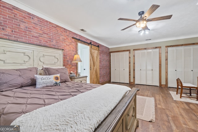 bedroom featuring crown molding, ceiling fan, a barn door, light hardwood / wood-style floors, and brick wall