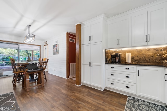 kitchen featuring pendant lighting, dark stone countertops, dark hardwood / wood-style floors, white cabinetry, and wood walls