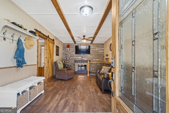 interior space featuring ceiling fan, wooden walls, a barn door, a fireplace, and dark hardwood / wood-style floors