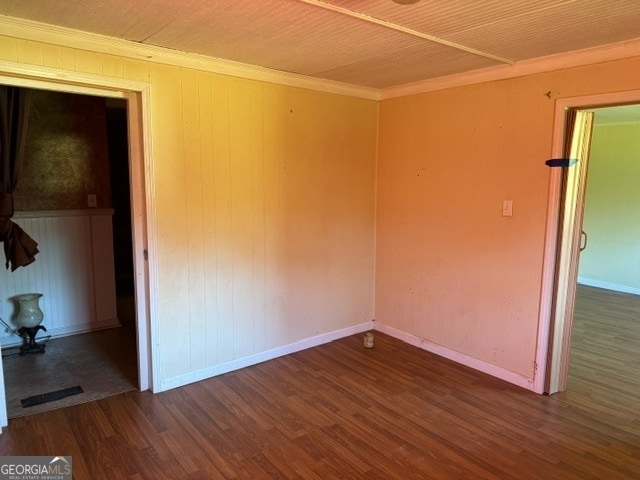 unfurnished room with crown molding, wooden walls, and dark wood-type flooring