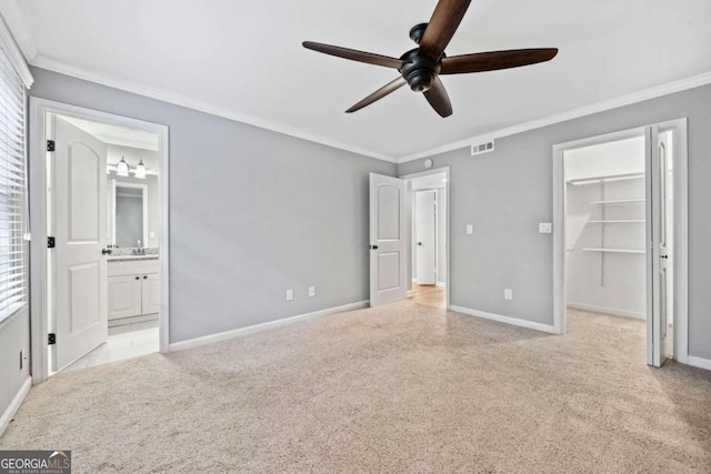 unfurnished bedroom with ceiling fan, a spacious closet, crown molding, and connected bathroom