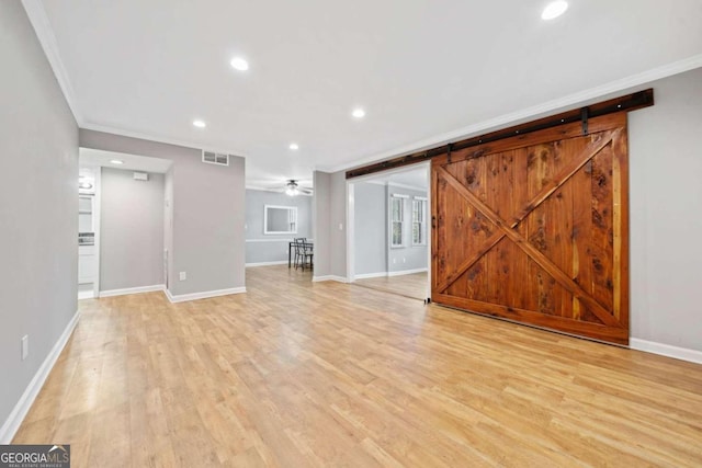 unfurnished living room with ceiling fan, a barn door, crown molding, and light hardwood / wood-style flooring