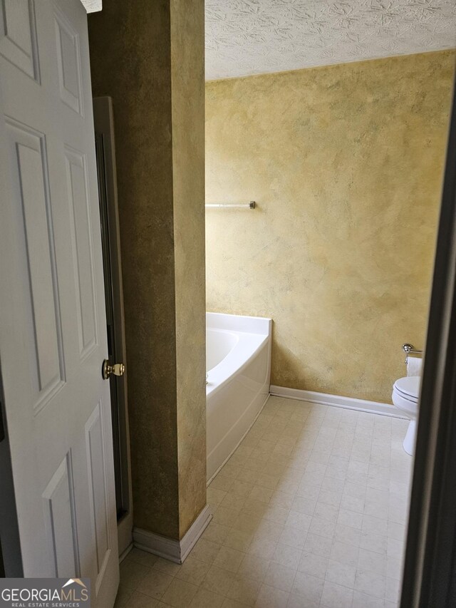 bathroom featuring a bath, a textured ceiling, and toilet