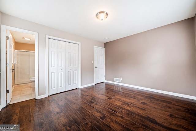 unfurnished bedroom featuring ensuite bathroom, dark hardwood / wood-style flooring, and a closet