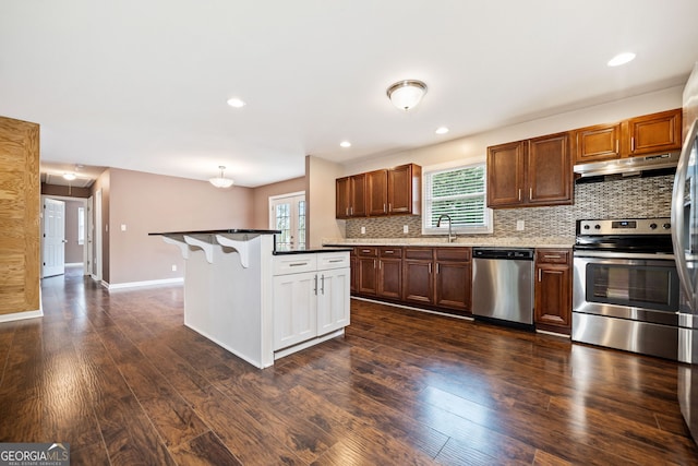 kitchen with a center island, sink, stainless steel appliances, dark hardwood / wood-style floors, and a breakfast bar area