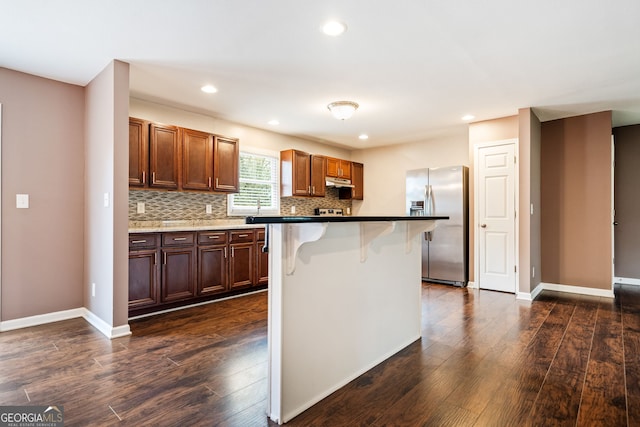 kitchen featuring decorative backsplash, stainless steel fridge, a breakfast bar, a center island, and dark hardwood / wood-style floors