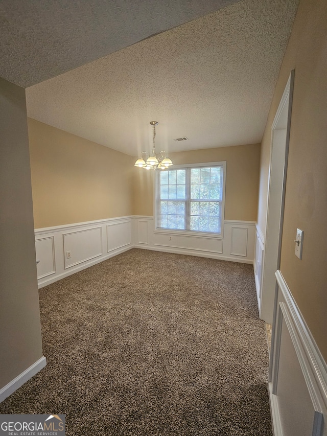 unfurnished room with a chandelier, dark carpet, and a textured ceiling