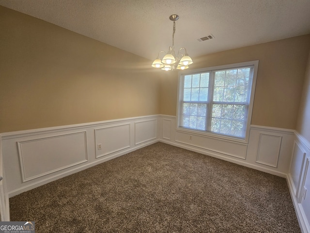 carpeted empty room featuring a textured ceiling and an inviting chandelier