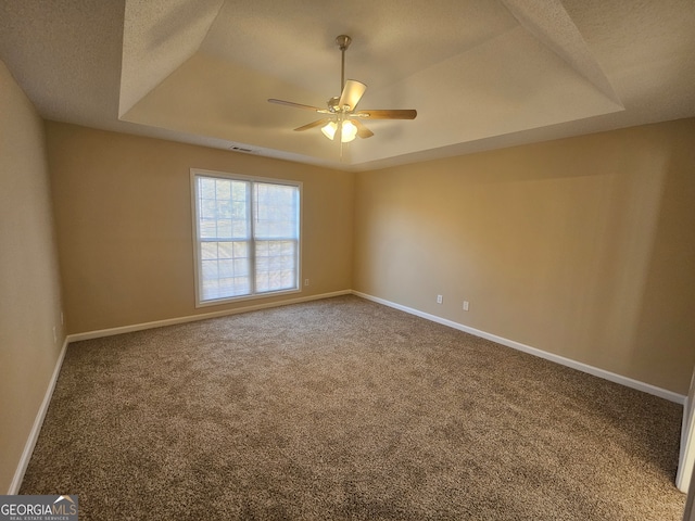 empty room featuring a tray ceiling, ceiling fan, carpet flooring, and a textured ceiling