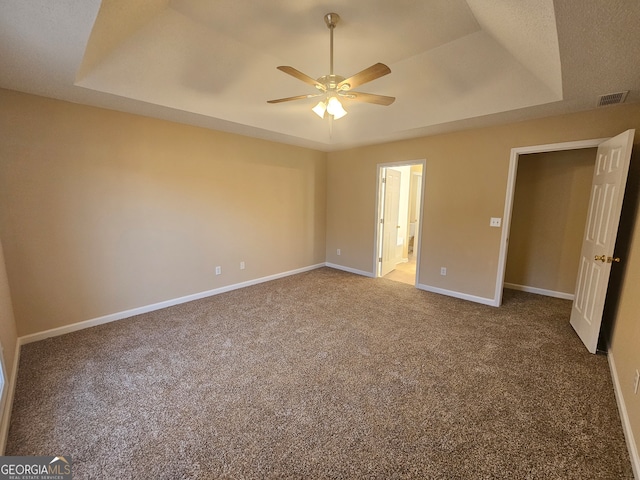 unfurnished bedroom with carpet flooring, ceiling fan, ensuite bathroom, and a tray ceiling