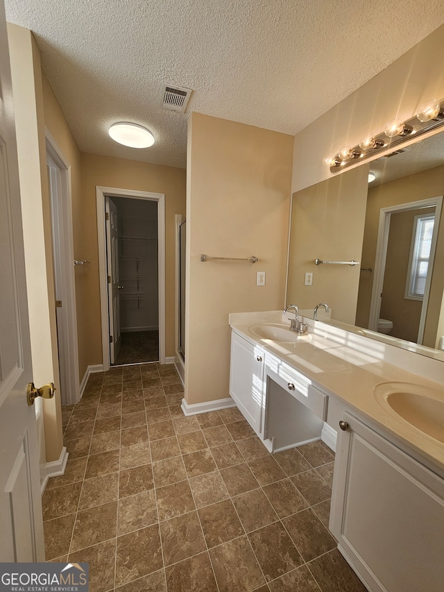 bathroom with vanity, a textured ceiling, toilet, and a shower with door