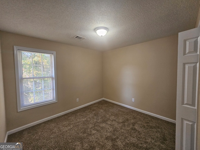 empty room featuring a textured ceiling and dark colored carpet