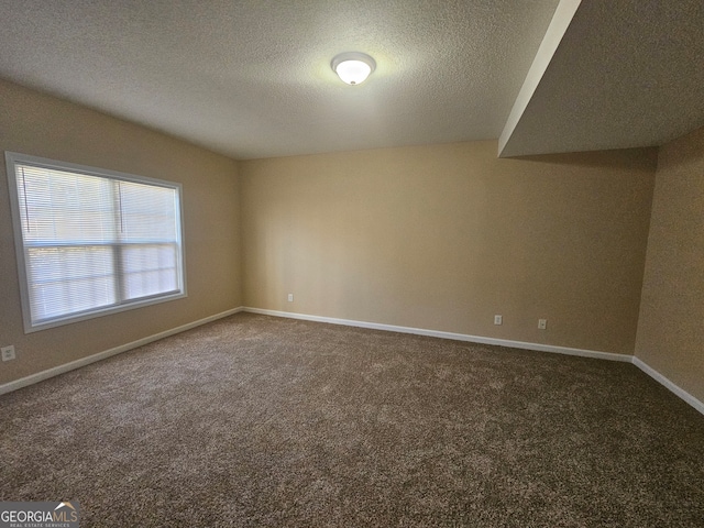 spare room featuring dark carpet and a textured ceiling