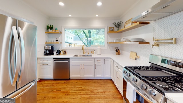 kitchen with appliances with stainless steel finishes, tasteful backsplash, sink, white cabinets, and range hood