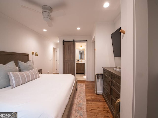 bedroom featuring ceiling fan, a barn door, dark wood-type flooring, and ensuite bath