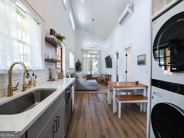 kitchen with gray cabinetry, sink, dark wood-type flooring, hanging light fixtures, and stacked washer / drying machine