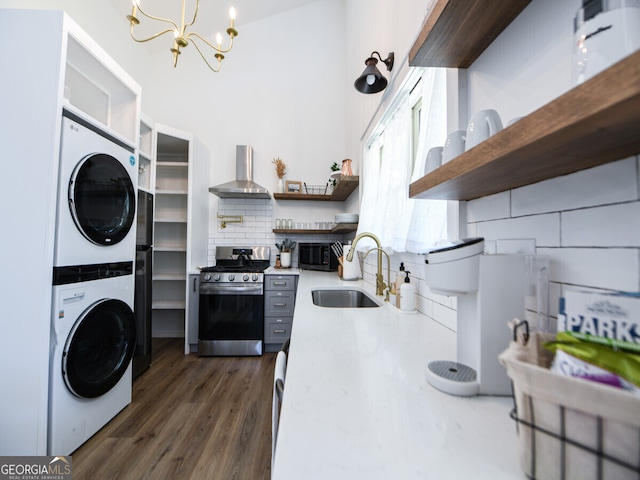 kitchen with sink, wall chimney range hood, a notable chandelier, stainless steel stove, and stacked washer and dryer