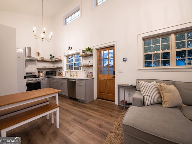 kitchen featuring wall chimney exhaust hood, stainless steel appliances, wood-type flooring, decorative light fixtures, and gray cabinets