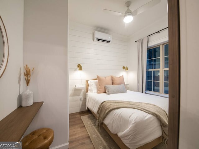 bedroom featuring a wall mounted air conditioner, hardwood / wood-style floors, and ceiling fan