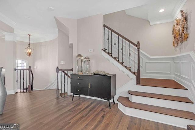 staircase with ornate columns, hardwood / wood-style floors, a notable chandelier, and ornamental molding