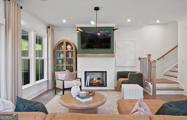 living room with light wood-type flooring, a brick fireplace, and crown molding