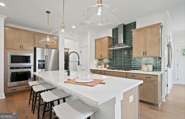 kitchen featuring stainless steel appliances, tasteful backsplash, a center island with sink, and wall chimney range hood