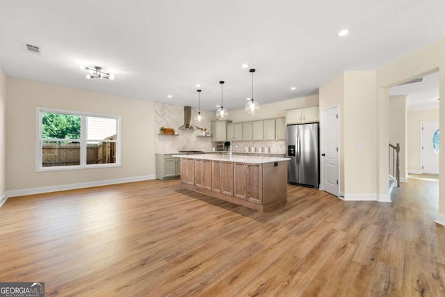 kitchen with pendant lighting, a center island with sink, light hardwood / wood-style flooring, wall chimney exhaust hood, and appliances with stainless steel finishes