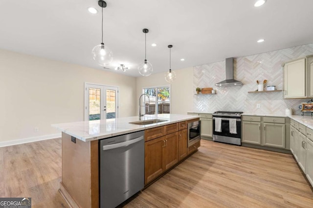 kitchen featuring wall chimney exhaust hood, light hardwood / wood-style flooring, decorative light fixtures, a kitchen island with sink, and appliances with stainless steel finishes