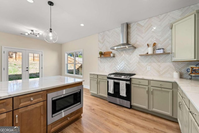 kitchen featuring pendant lighting, light hardwood / wood-style floors, wall chimney range hood, and stainless steel appliances