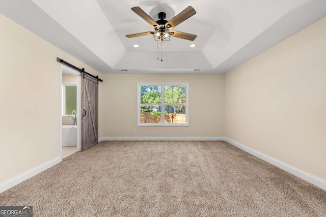 carpeted spare room featuring a barn door, a raised ceiling, and ceiling fan