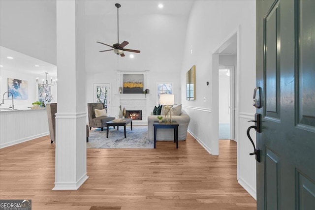 entrance foyer featuring a stone fireplace, ceiling fan with notable chandelier, light hardwood / wood-style floors, and a high ceiling