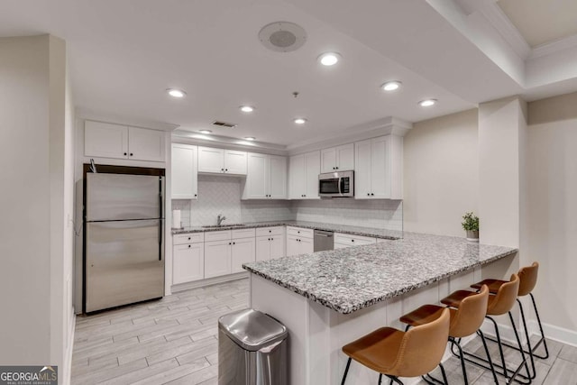 kitchen with appliances with stainless steel finishes, kitchen peninsula, sink, and white cabinets