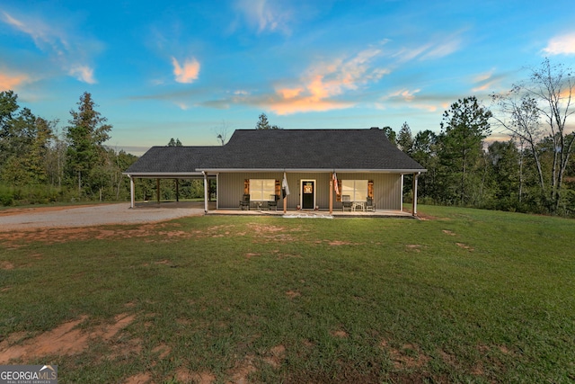 back house at dusk with covered porch, a carport, and a lawn