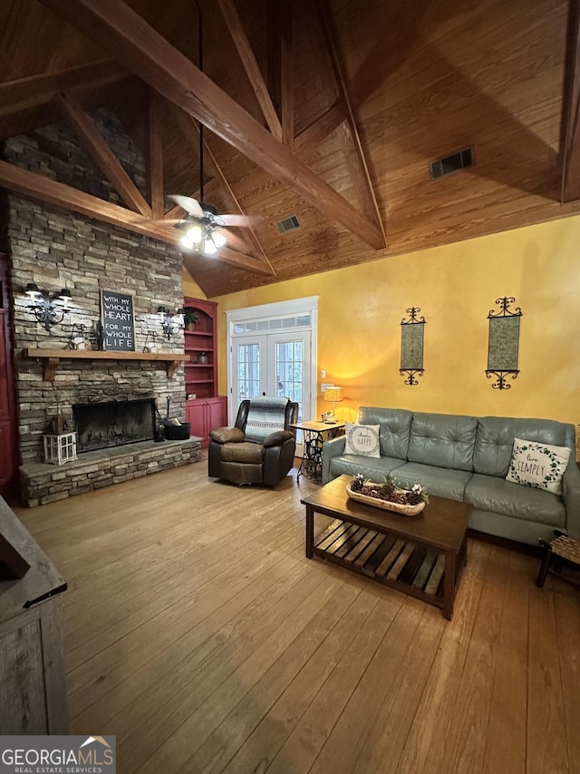 living room with built in shelves, ceiling fan, wooden ceiling, a stone fireplace, and beamed ceiling