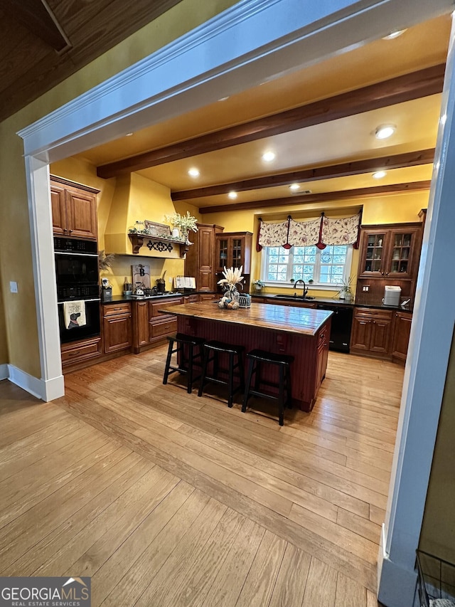 bar with beam ceiling, black double oven, light hardwood / wood-style floors, and sink