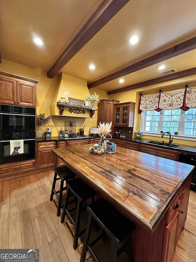 kitchen with sink, beamed ceiling, wooden counters, black appliances, and light wood-type flooring