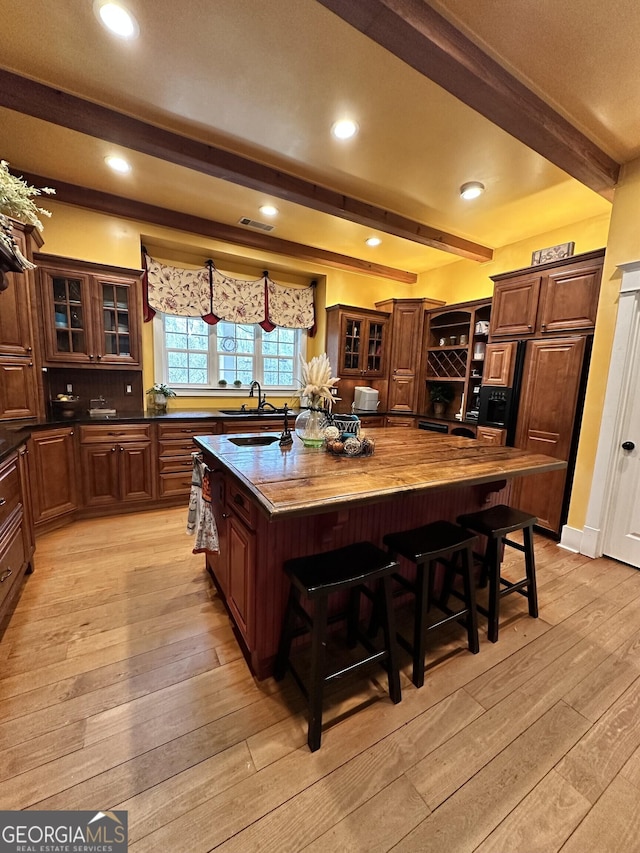 kitchen with a kitchen bar, beam ceiling, light hardwood / wood-style flooring, and a kitchen island with sink