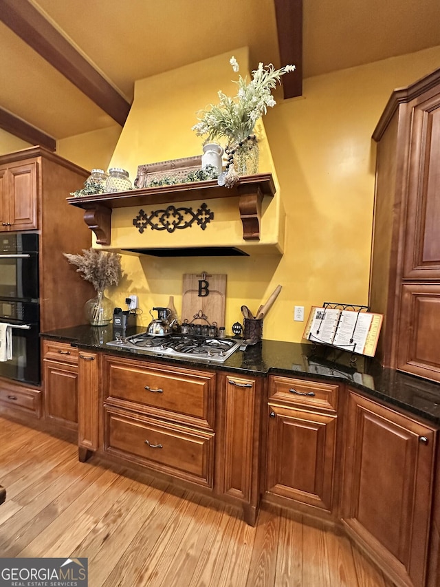 bar featuring double oven, dark stone counters, light wood-type flooring, and stainless steel gas cooktop