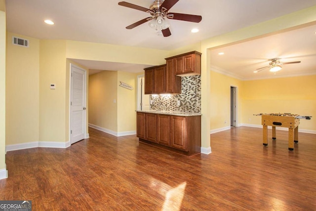 kitchen with dark wood-type flooring, ceiling fan, crown molding, and decorative backsplash