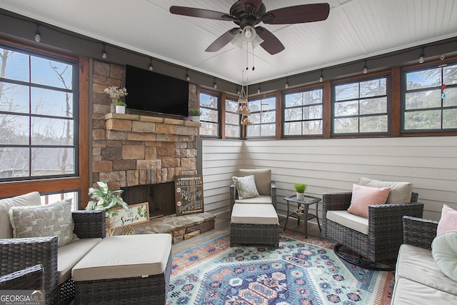 living room with ceiling fan, a stone fireplace, and a wealth of natural light