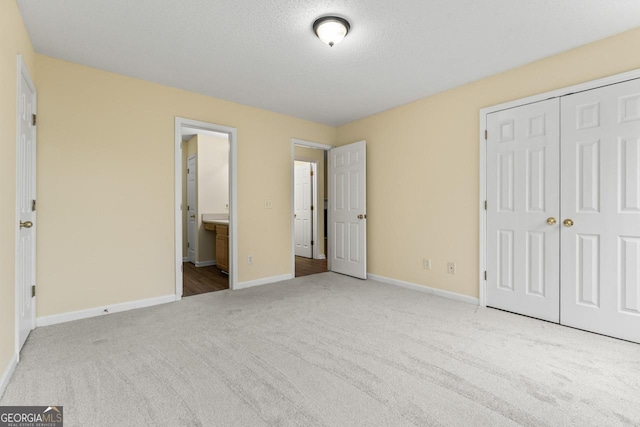 unfurnished bedroom featuring a textured ceiling, ensuite bathroom, carpet flooring, baseboards, and a closet