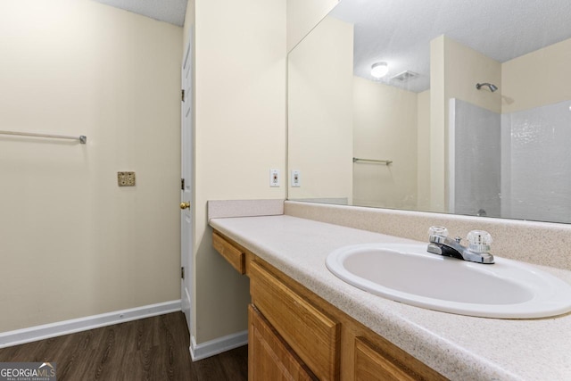 bathroom with a textured ceiling, wood finished floors, vanity, and baseboards