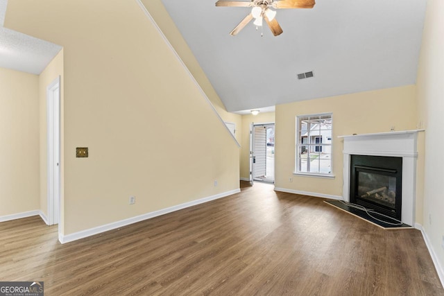 unfurnished living room featuring visible vents, a glass covered fireplace, vaulted ceiling, wood finished floors, and baseboards