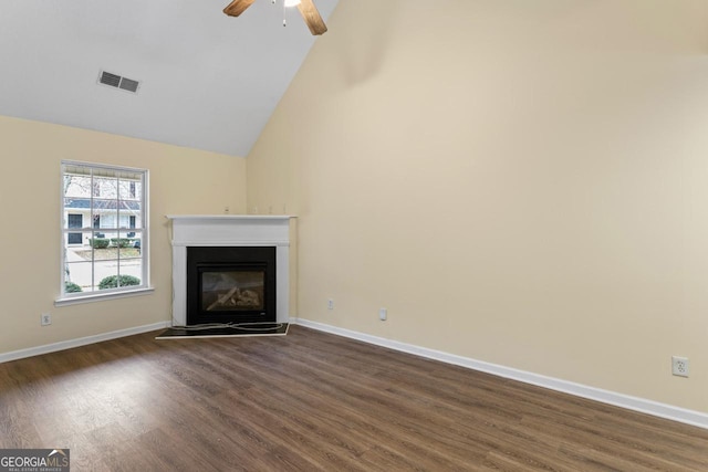 unfurnished living room with baseboards, visible vents, a glass covered fireplace, dark wood-type flooring, and high vaulted ceiling