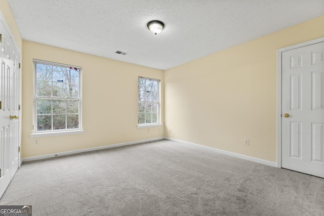 spare room featuring a textured ceiling, carpet floors, visible vents, and baseboards