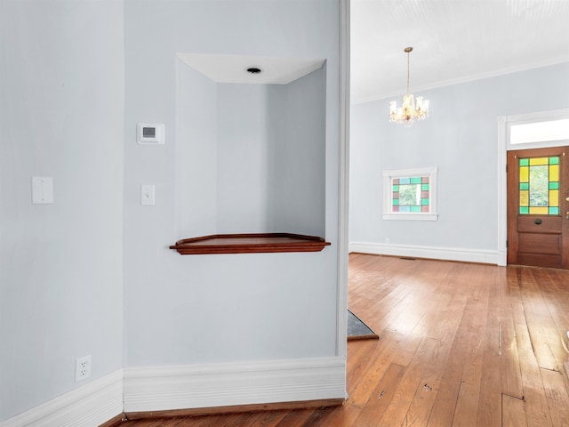 corridor with crown molding, light hardwood / wood-style flooring, and an inviting chandelier