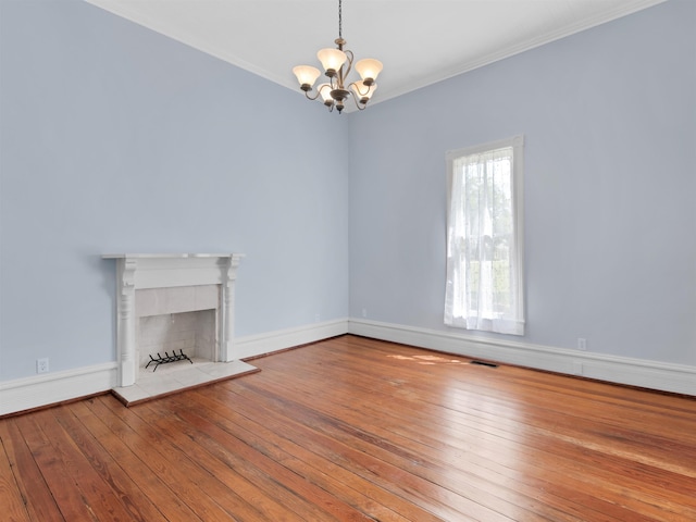 unfurnished living room featuring a tile fireplace, hardwood / wood-style floors, ornamental molding, and a notable chandelier