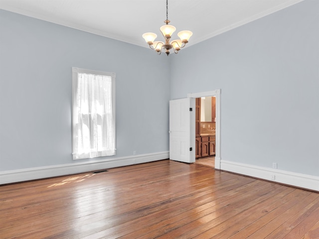 empty room featuring a chandelier, hardwood / wood-style floors, and crown molding