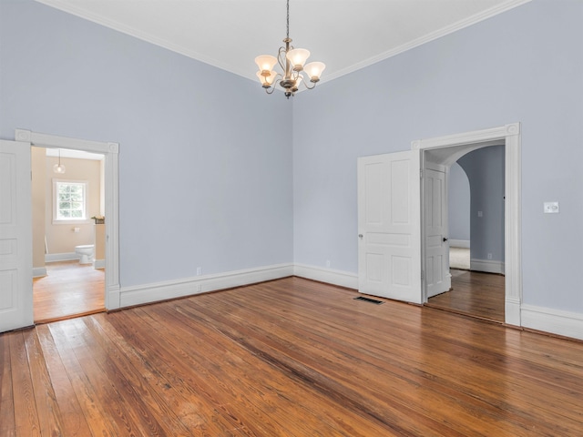 spare room with hardwood / wood-style floors, an inviting chandelier, and crown molding