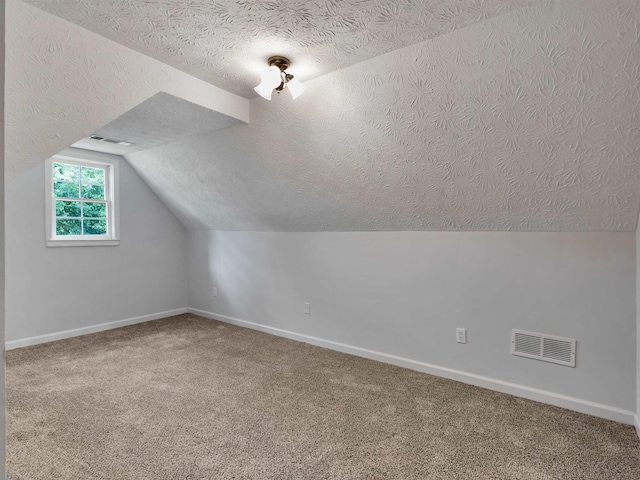 additional living space featuring lofted ceiling, carpet, and a textured ceiling